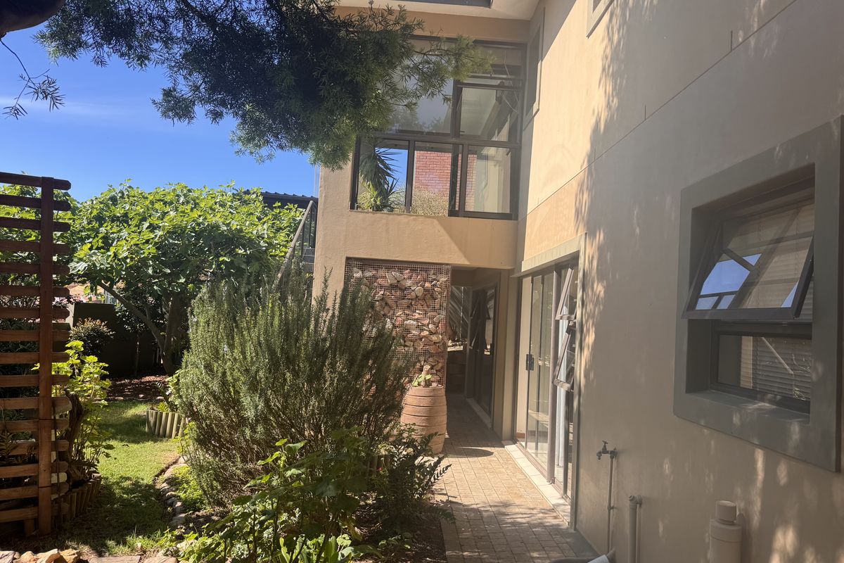 Rear exterior view showing a paved walkway, stone gabion feature, and access to the home via sliding glass doors and large windows.