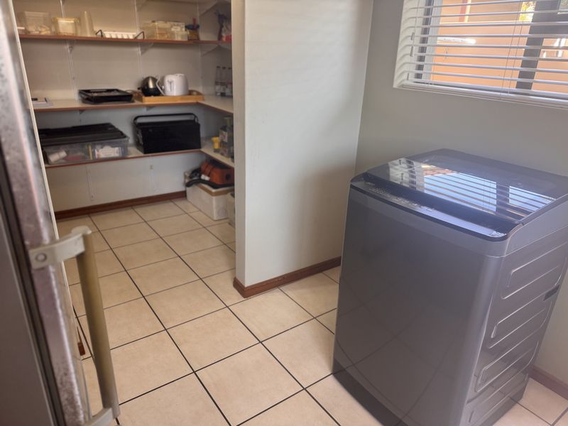 A functional scullery or utility area featuring built-in shelving for storage, tiled flooring, and a window with venetian blinds.