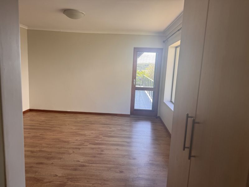 A bright, empty bedroom featuring laminate flooring, a built-in cupboard, and a glass-paneled door providing access to an outdoor area.