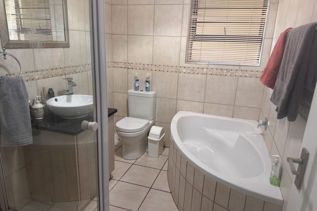A functional bathroom featuring a corner bathtub, vanity with vessel sink, toilet, and neutral wall and floor tiling.
