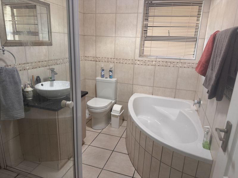 A functional bathroom featuring a corner bathtub, vanity with vessel sink, toilet, and neutral wall and floor tiling.