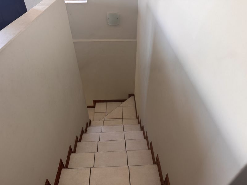 A view looking down a tiled staircase with a wall-mounted light fixture in a neutral hallway setting.
