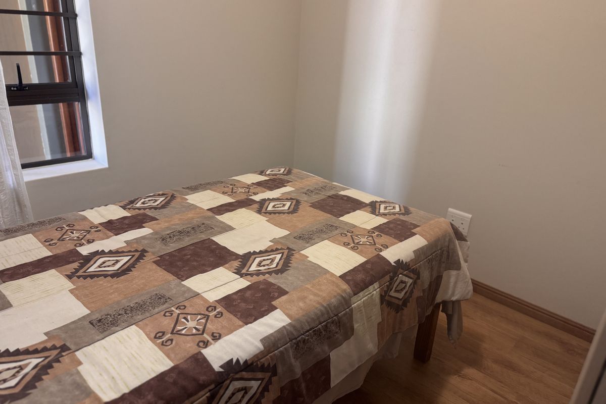 A functional bedroom featuring laminate flooring, a window with security bars, and neutral wall finishes.