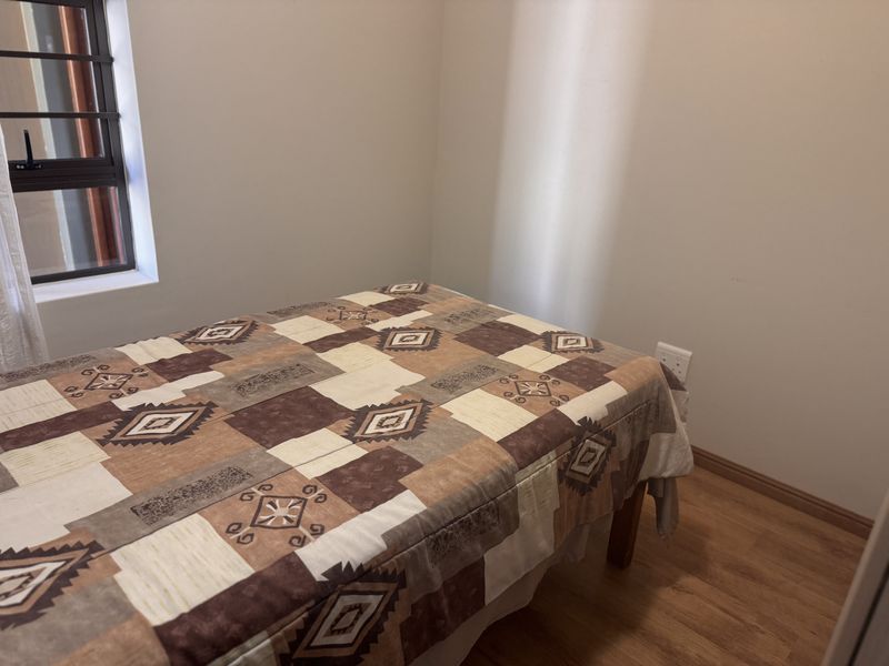 A functional bedroom featuring laminate flooring, a window with security bars, and neutral wall finishes.