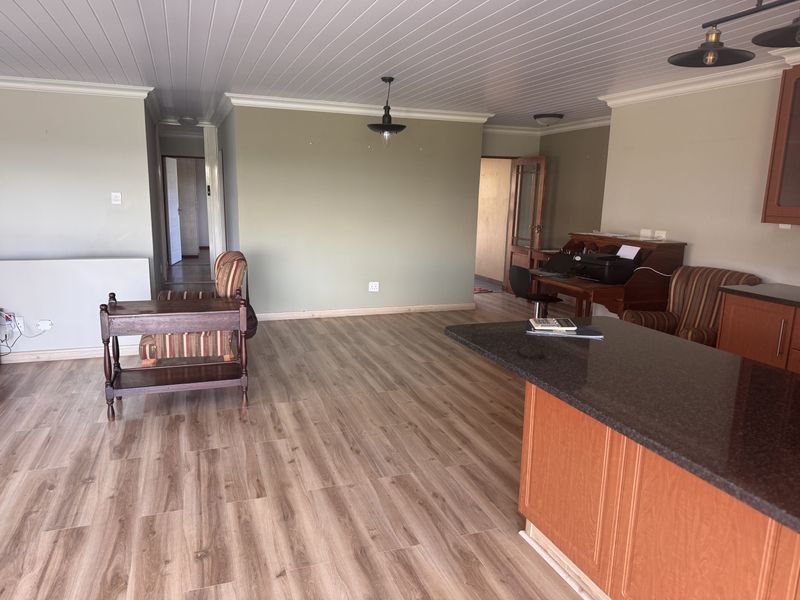 Spacious open-plan living area featuring modern laminate flooring, a granite-topped kitchen island, and a classic tongue and groove ceiling.