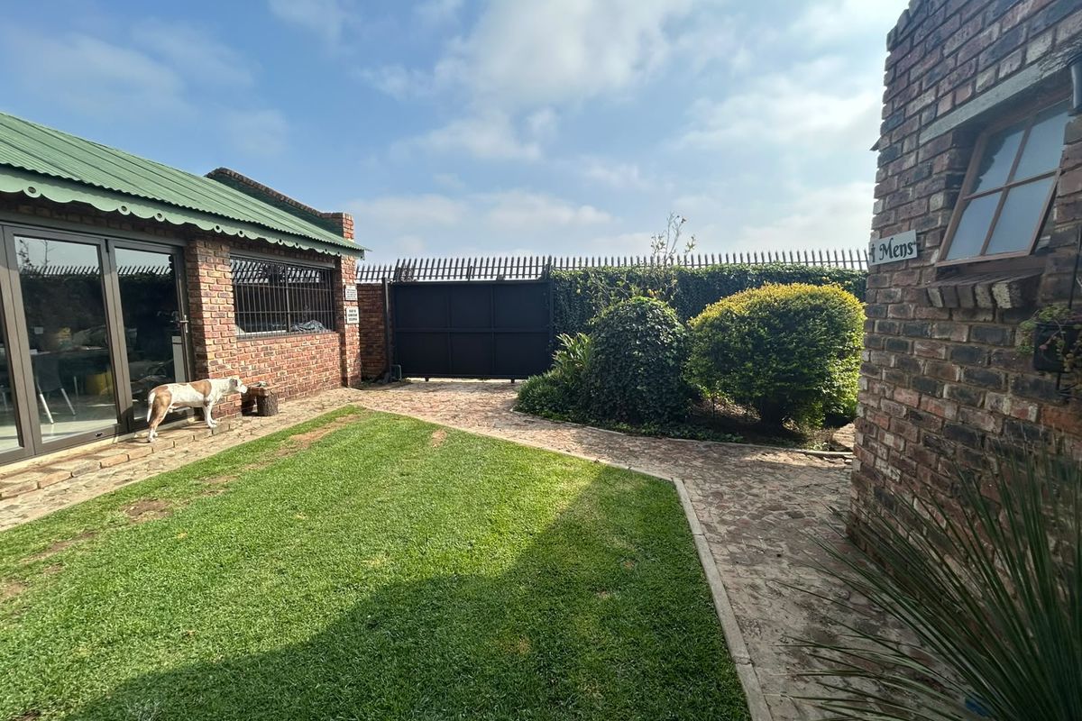 A well-maintained rear courtyard featuring face brick structures, a green corrugated roof, paved pathways, and a manicured lawn area.