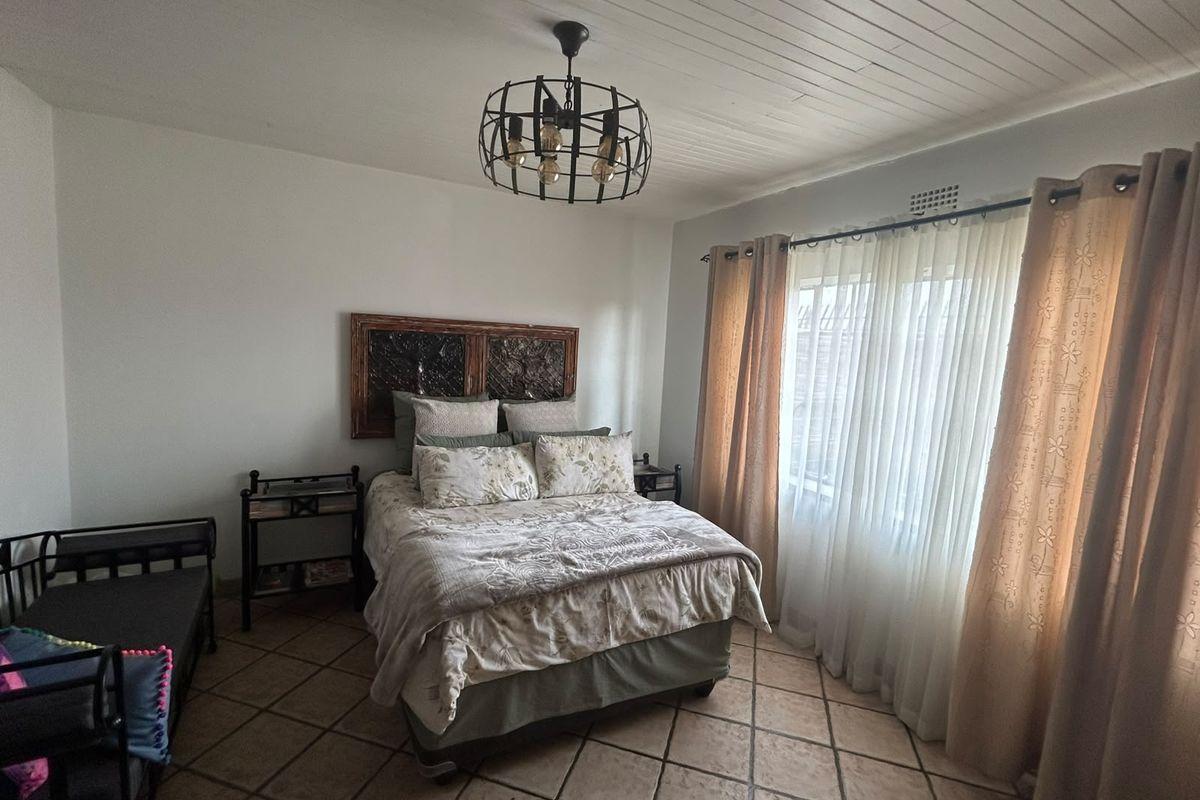 A well-lit bedroom featuring tiled flooring, a distinctive tongue and groove ceiling, and a central metal pendant light fixture.
