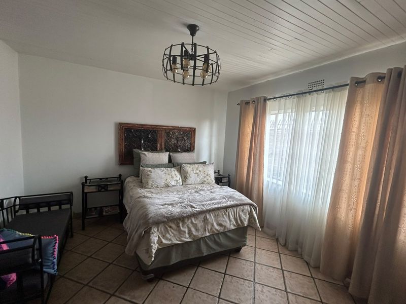 A well-lit bedroom featuring tiled flooring, a distinctive tongue and groove ceiling, and a central metal pendant light fixture.
