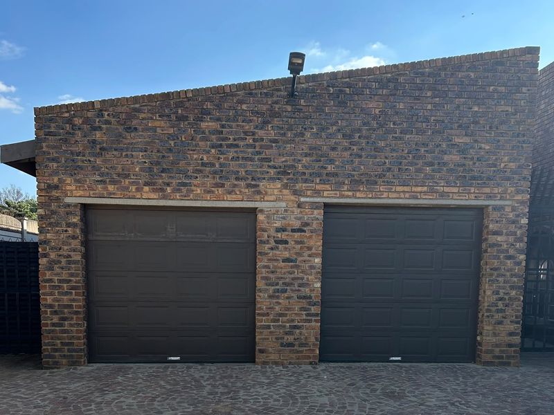 A double garage featuring a durable face brick exterior and two dark-toned sectional garage doors, set against a paved driveway.