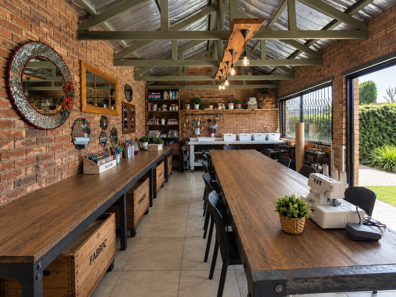 A spacious, well-lit utility or craft room featuring exposed brick walls, timber roof trusses, tiled floors, and large sliding doors opening to the garden.
