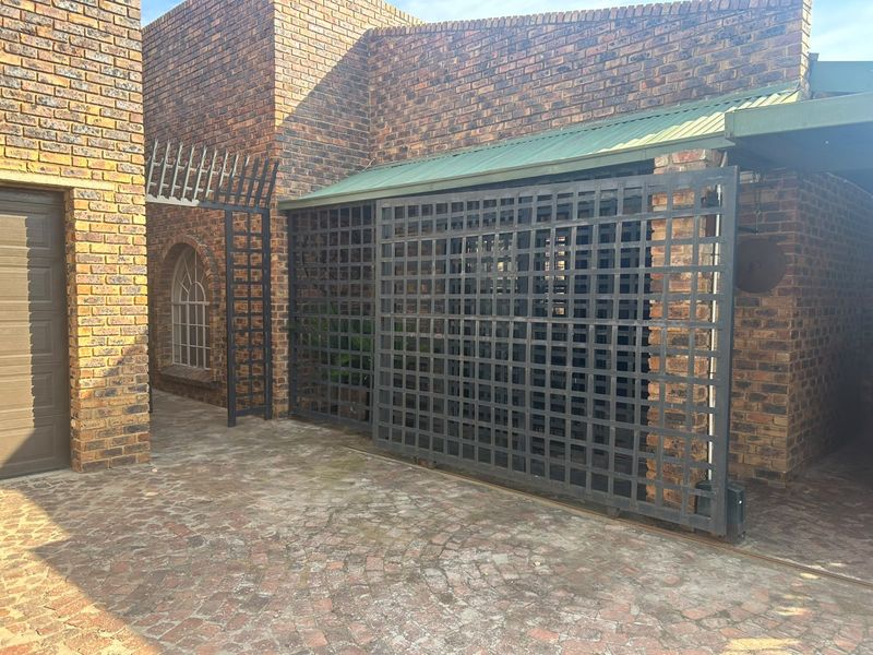Front exterior view featuring face brick construction, a paved driveway, a garage entrance, and a sliding security gate.