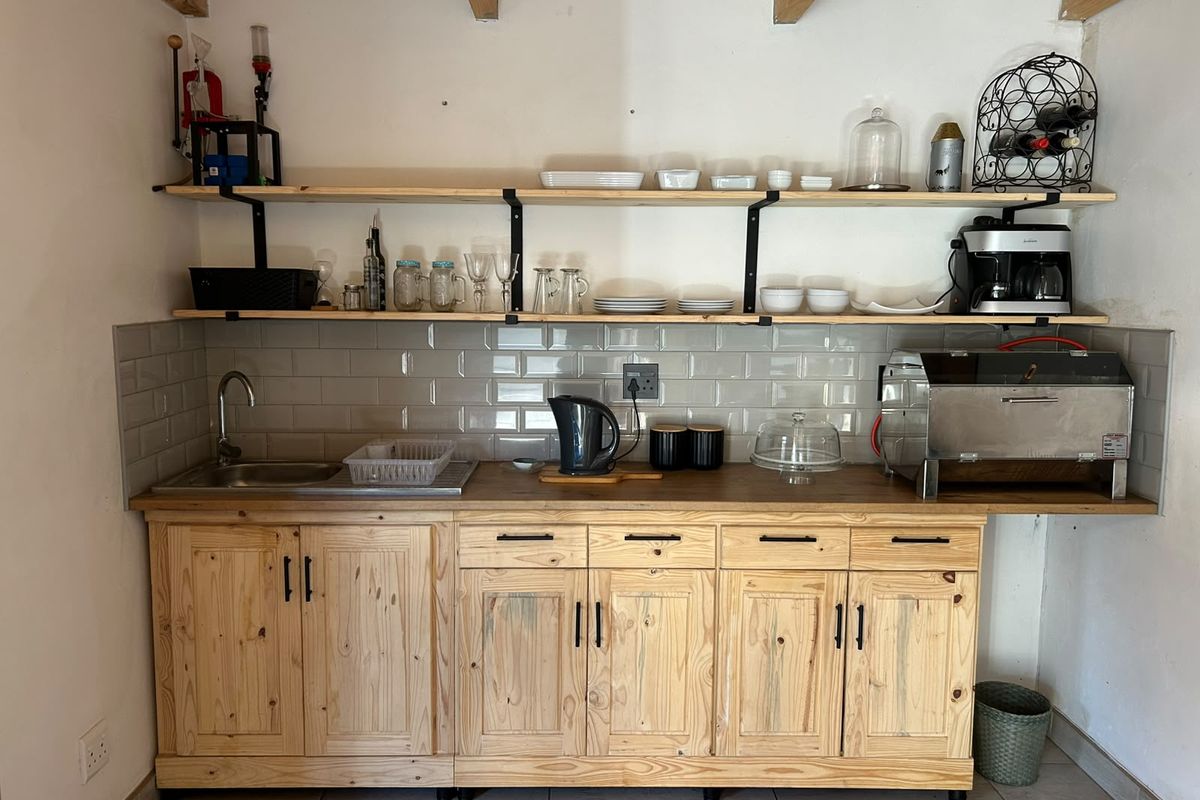 A rustic-style kitchen kitchenette featuring natural wood cabinetry, open shelving, a subway tile backsplash, and exposed ceiling beams.
