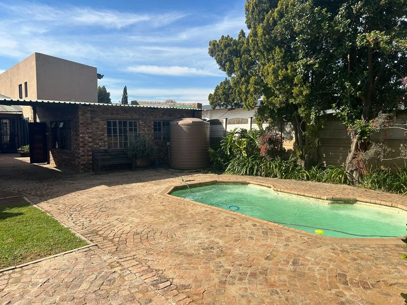 Outdoor pool area featuring brick paving, a water storage tank, and established garden surroundings.