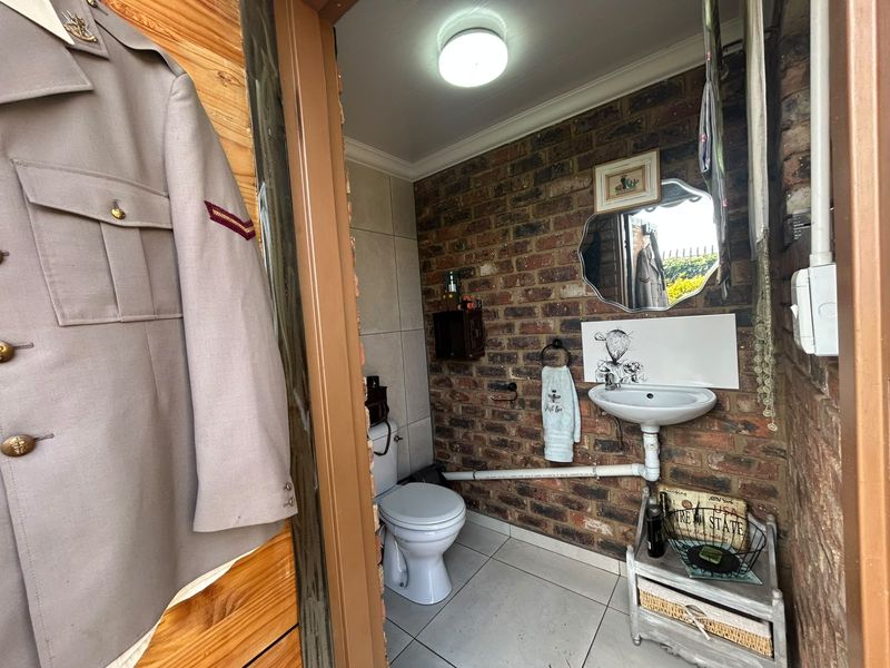 A compact bathroom featuring exposed brick walls, ceramic floor tiles, a wall-mounted basin, and a standard toilet.