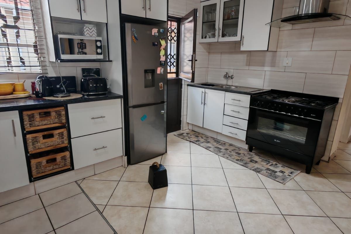 A functional kitchen featuring white cabinetry, a stainless steel extractor fan, a black gas stove, and tiled flooring with a neutral backsplash.