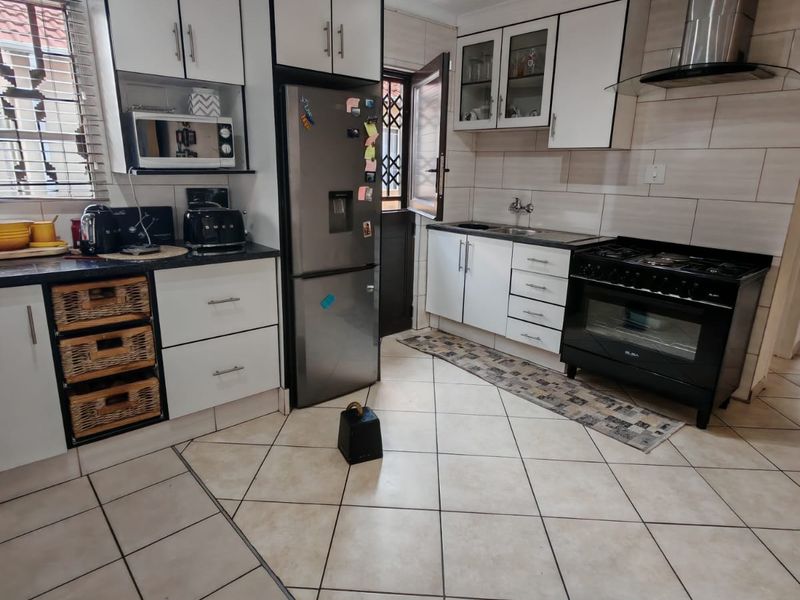 A functional kitchen featuring white cabinetry, a stainless steel extractor fan, a black gas stove, and tiled flooring with a neutral backsplash.