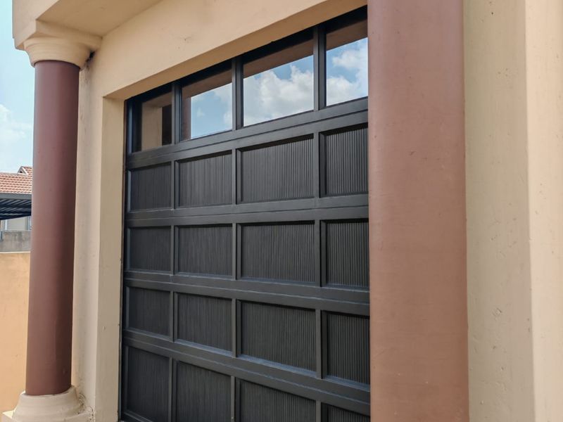 A secure sectional garage door framed by decorative columns, featuring a durable finish and a paved driveway approach.
