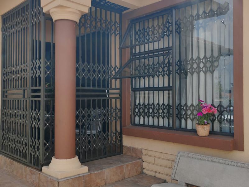Front entrance area featuring tiled steps, a structural column, and security gates and bars installed on the windows and doorway.