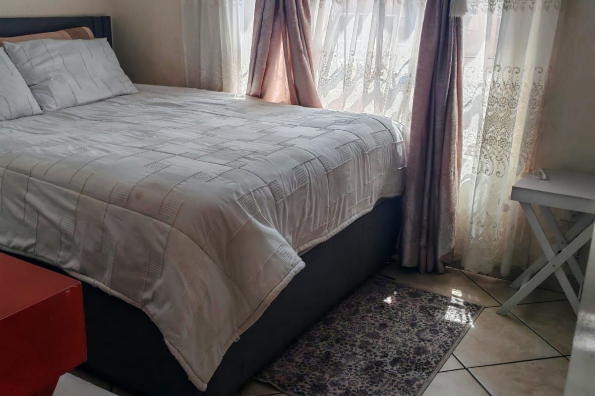 A bedroom featuring tiled flooring and a window fitted with security bars, offering natural light.