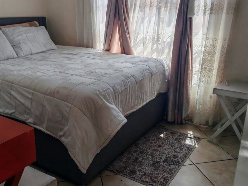 A bedroom featuring tiled flooring and a window fitted with security bars, offering natural light.
