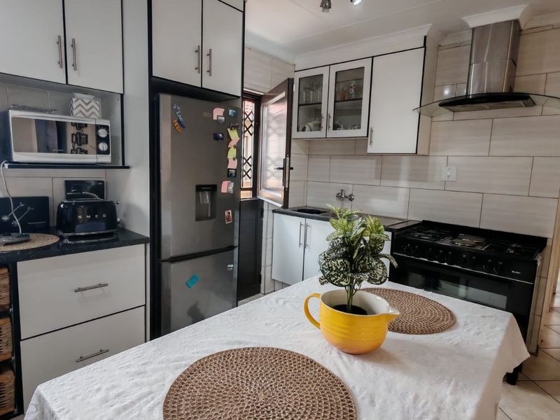 A functional kitchen featuring white cabinetry, stainless steel appliances, a gas hob with extractor fan, tiled backsplash, and neutral floor tiles.