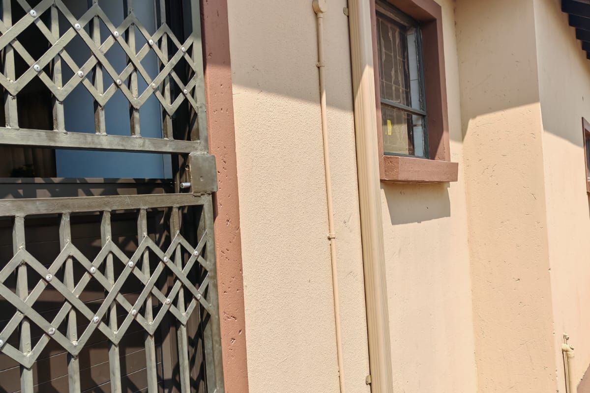 A side view of the property exterior featuring a security gate, downpipe, and brick paved walkway.