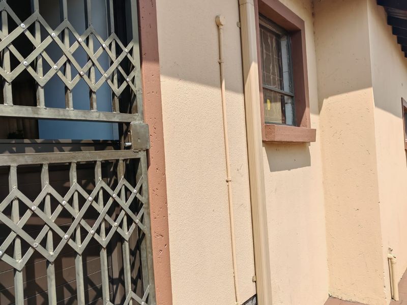 A side view of the property exterior featuring a security gate, downpipe, and brick paved walkway.