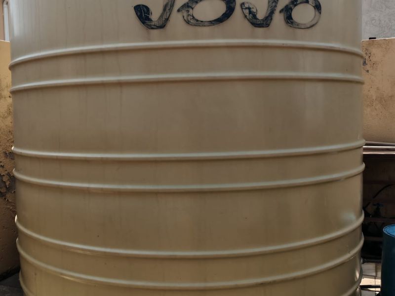 A large beige water storage tank situated on a tiled outdoor utility area.