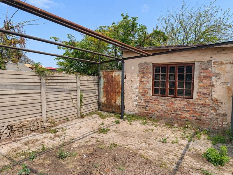 Rear outdoor area featuring a paved patio, precast boundary wall, and a metal pergola structure attached to a brick building with weathered finishes.