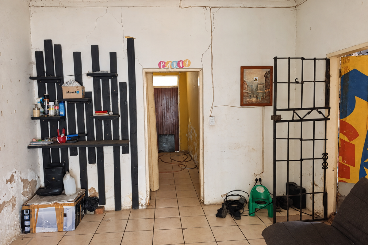 Living area featuring ceramic floor tiles and a security gate, currently showing significant wall cracking and plaster damage requiring maintenance and repair.
