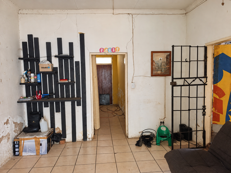 Living area featuring ceramic floor tiles and a security gate, currently showing significant wall cracking and plaster damage requiring maintenance and repair.