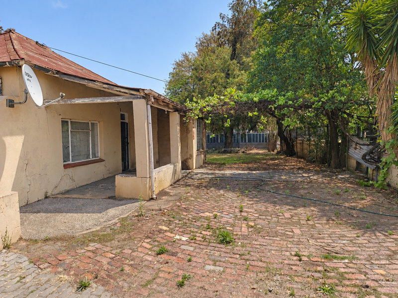 Rear exterior view of the property featuring a covered patio, brick paving, and significant signs of wear on the roof and exterior walls.