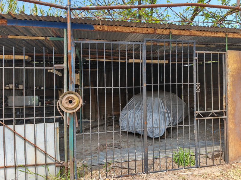 A basic, utilitarian garage structure featuring a corrugated metal roof and a secure metal gate enclosure.