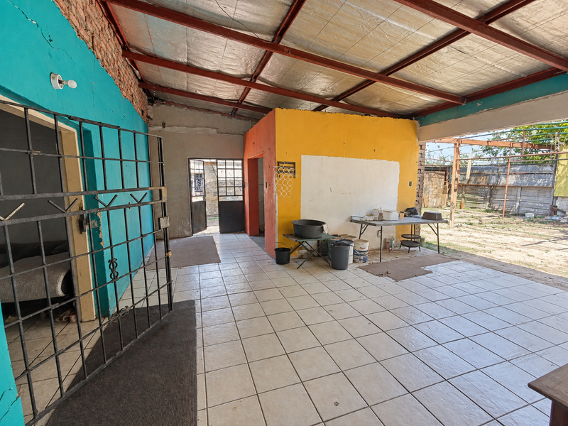An expansive, semi-enclosed patio area featuring tiled flooring, exposed steel roof beams, and vibrant painted walls, offering potential for outdoor living development.