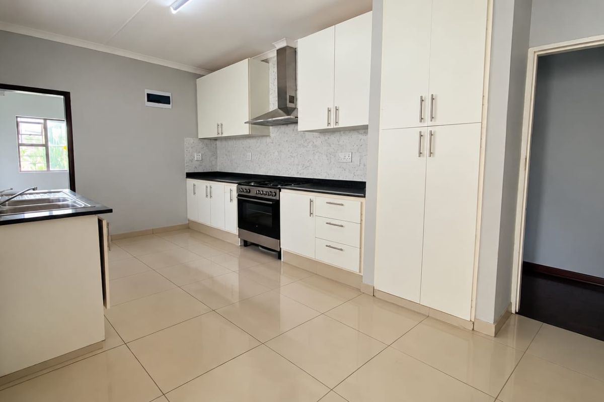 Modern kitchen featuring white cabinetry, stone countertops, a gas stove with extractor fan, and tiled flooring in a clean, open layout.