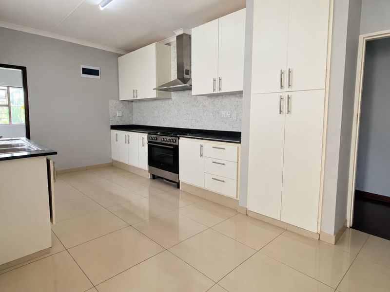 Modern kitchen featuring white cabinetry, stone countertops, a gas stove with extractor fan, and tiled flooring in a clean, open layout.