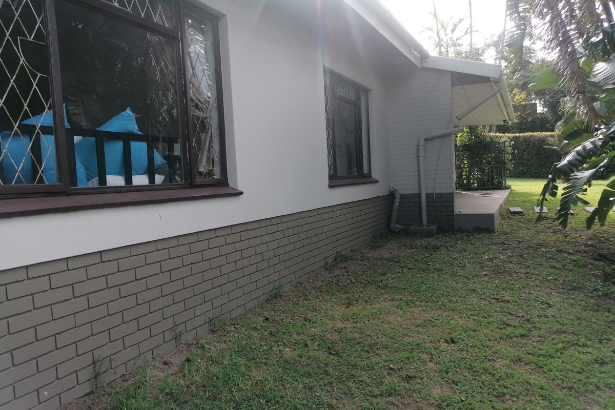 Rear exterior view of the house featuring a brick plinth, leaded glass windows, and a small covered patio area overlooking the garden.