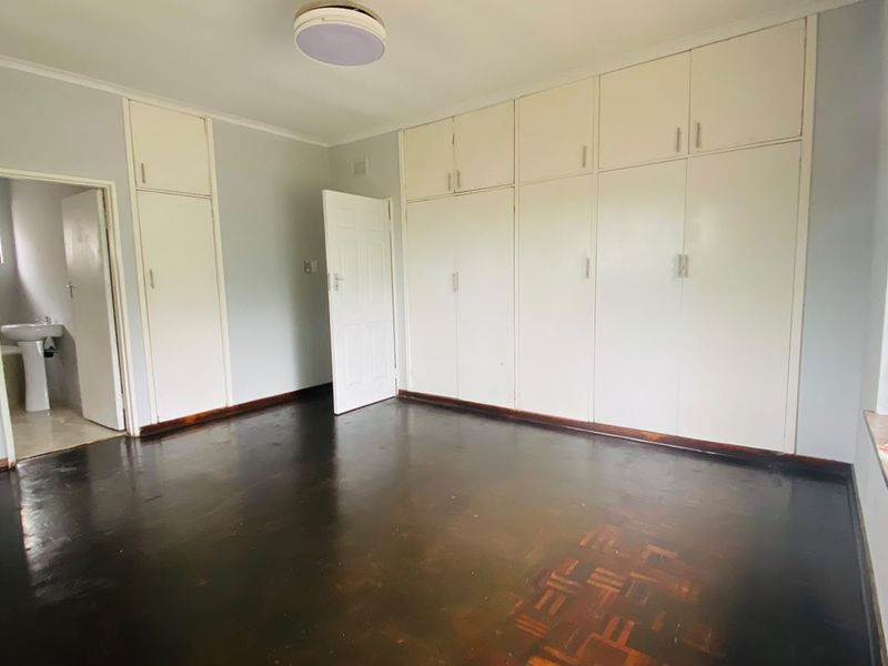 Spacious bedroom featuring dark parquet flooring, extensive built-in cupboard storage, and an en-suite bathroom access.