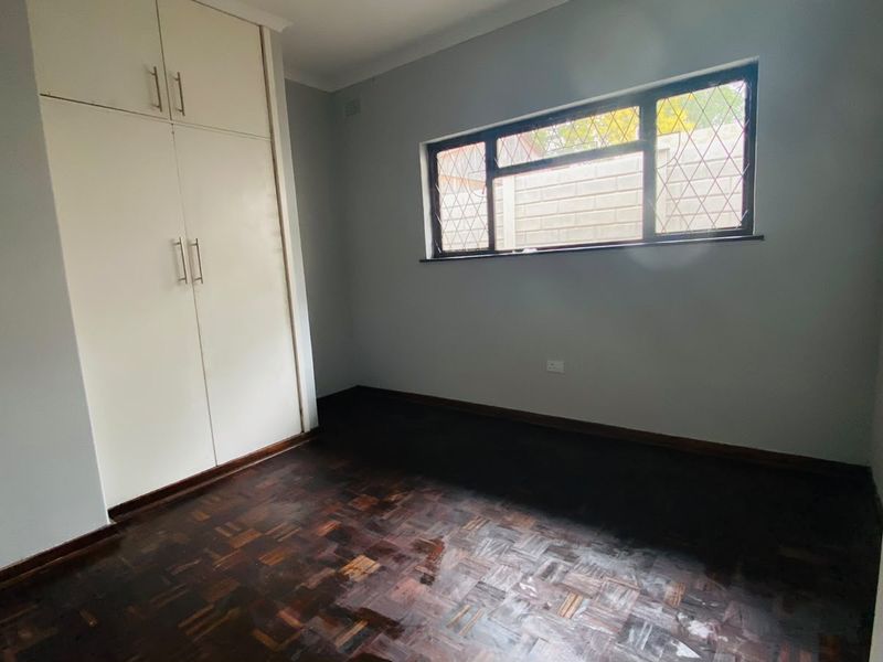 An empty bedroom featuring dark parquet flooring, built-in cupboards, and a window with security bars.