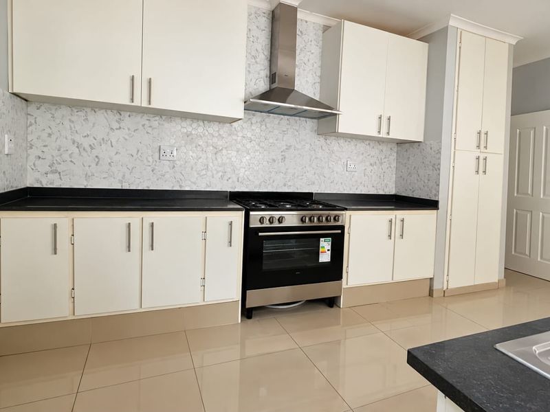 Modern kitchen featuring white cabinetry, stone countertops, a mosaic backsplash, and a stainless steel gas stove with an extractor fan.