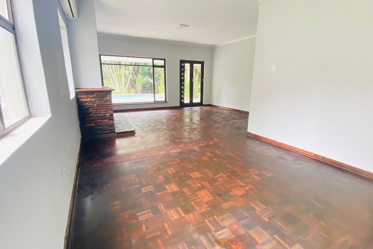 Spacious living area featuring classic parquet flooring, a brick fireplace, and large windows providing natural light and views of the garden and pool area.