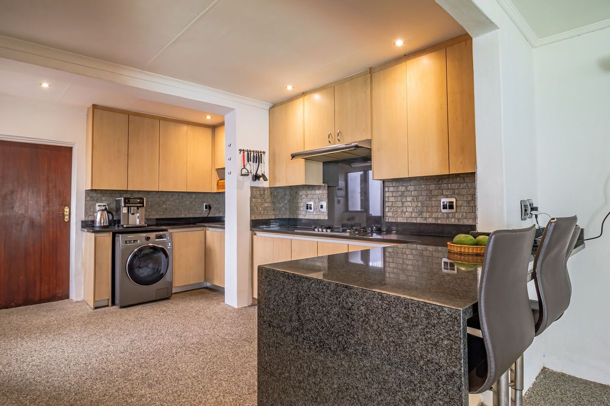 A functional kitchen featuring light wood cabinetry, dark granite countertops, a breakfast bar, and integrated appliances with a tiled backsplash.