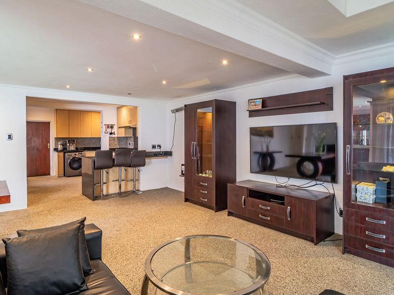 Spacious open-plan living area featuring a connected kitchen with breakfast bar, recessed lighting, and neutral carpeting throughout.