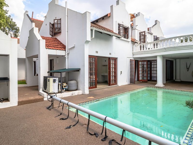 Rear exterior view featuring a swimming pool, built-in braai area, and a covered terrace with classic architectural columns and a balcony above.