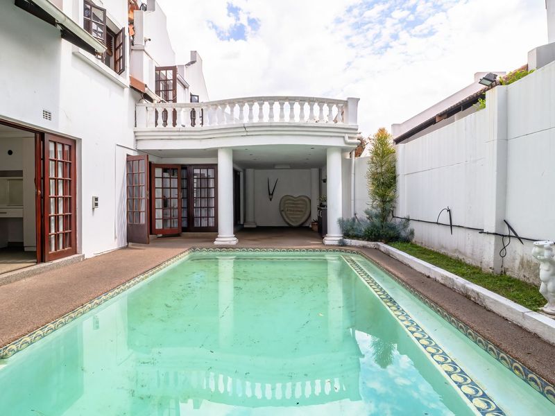 Outdoor pool area featuring a covered patio with classic columns, balustrade detailing, and direct access to the home through multiple sets of french doors.