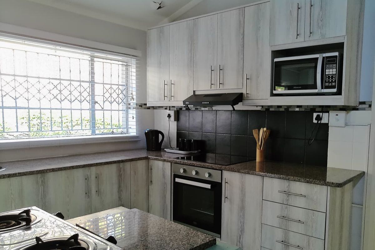 A functional kitchen featuring light wood-grain cabinetry, granite countertops, a tiled backsplash, and integrated appliances including an oven, hob, and microwave.