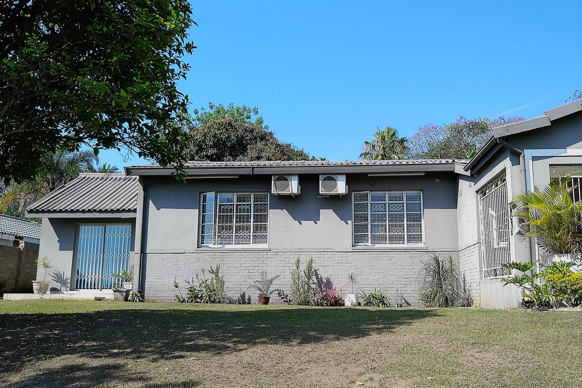 Rear view of the house featuring a brick facade, tiled roof, security-barred windows, and installed air conditioning units overlooking a garden area.