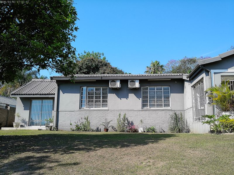 Rear view of the house featuring a brick facade, tiled roof, security-barred windows, and installed air conditioning units overlooking a garden area.