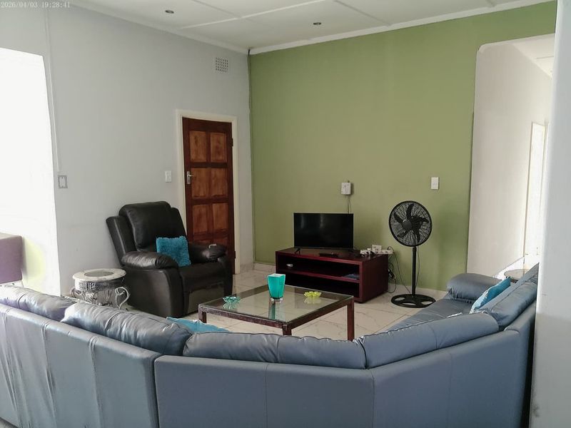 A living room featuring tiled flooring, a green accent wall, and a wooden door, providing a functional space for relaxation.