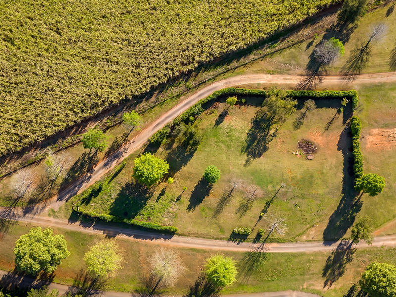 Aerial view of a vacant residential plot featuring established trees, hedgerow boundaries, and access via an unpaved road.